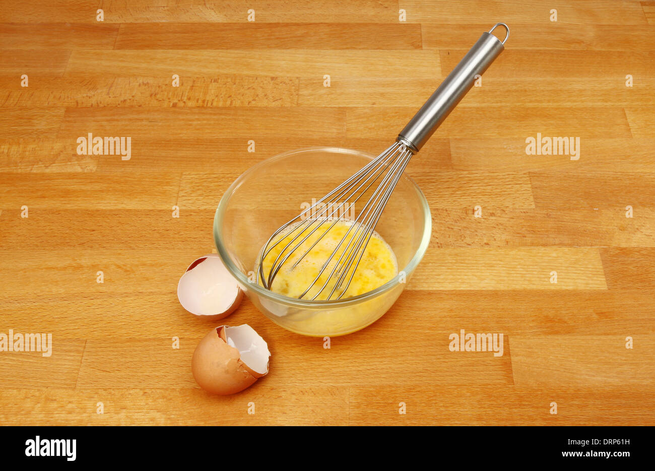 Eggs and a whisk in a glass mixing bowl with egg shells on a wooden kitchen worktop Stock Photo