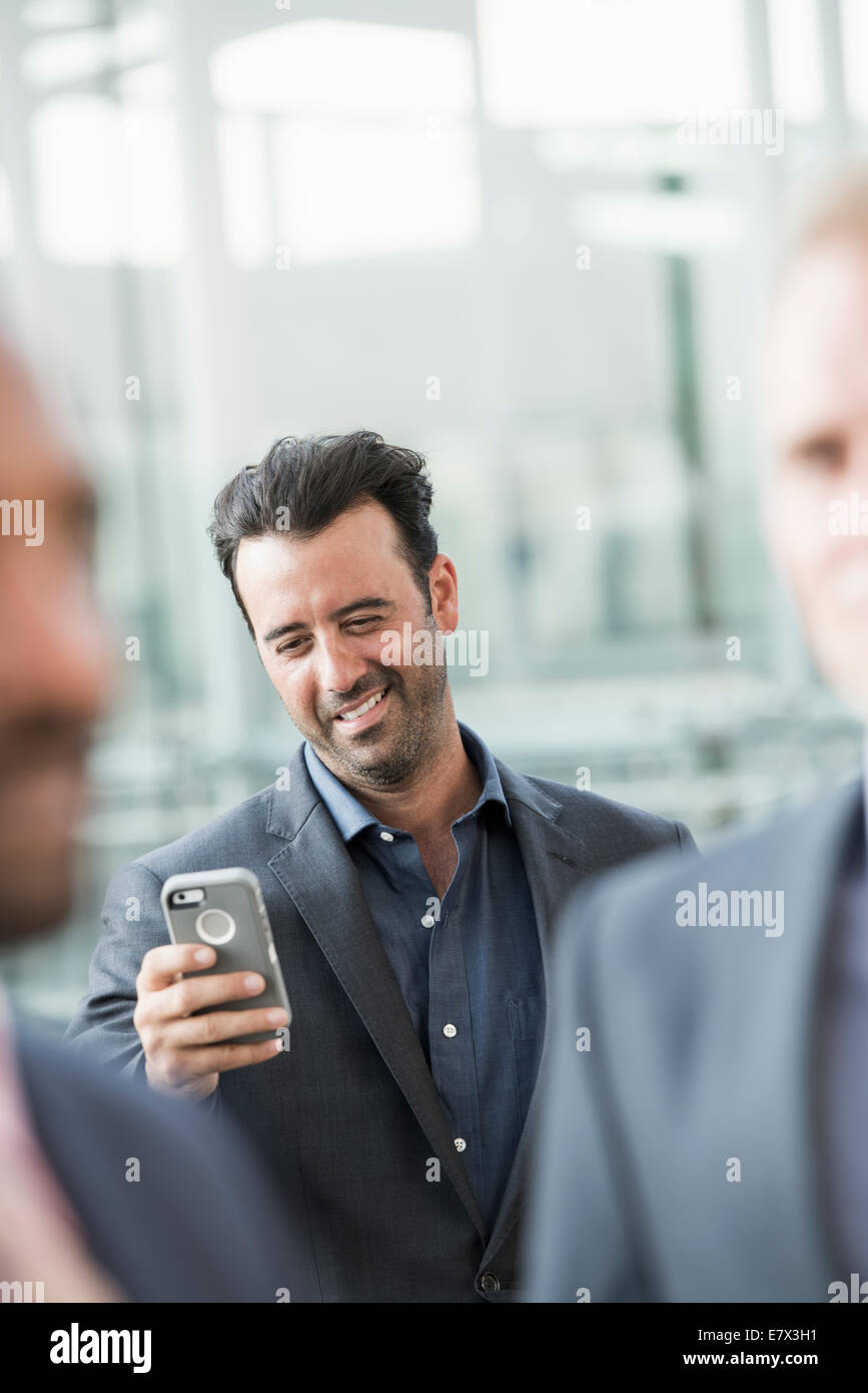 Three businessmen, one checking his smart phone. Stock Photo