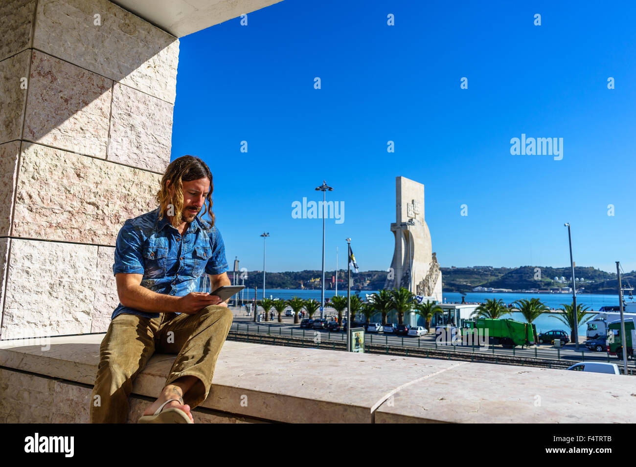 Man reads from an electronic tablet in front of the Portuguese icon, Monument to the Discoveries Padrao dos Descobrimentos. Stock Photo