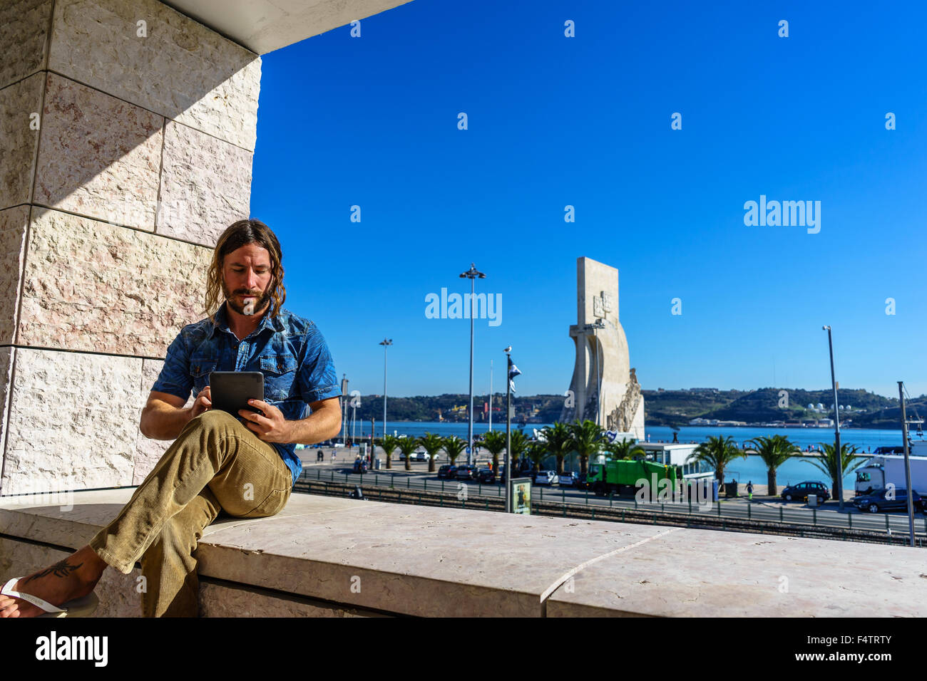 Man reads from an electronic tablet in front of the Portuguese icon, Monument to the Discoveries Padrao dos Descobrimentos. Stock Photo