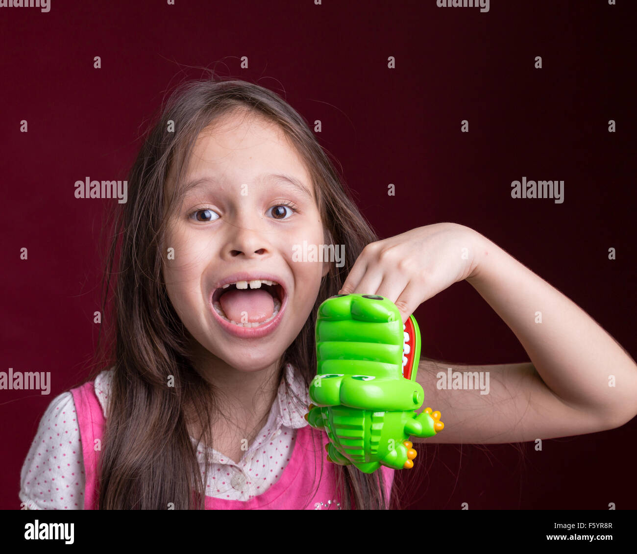 Young Asian American girl with green crocodile toy biting hand Stock Photo