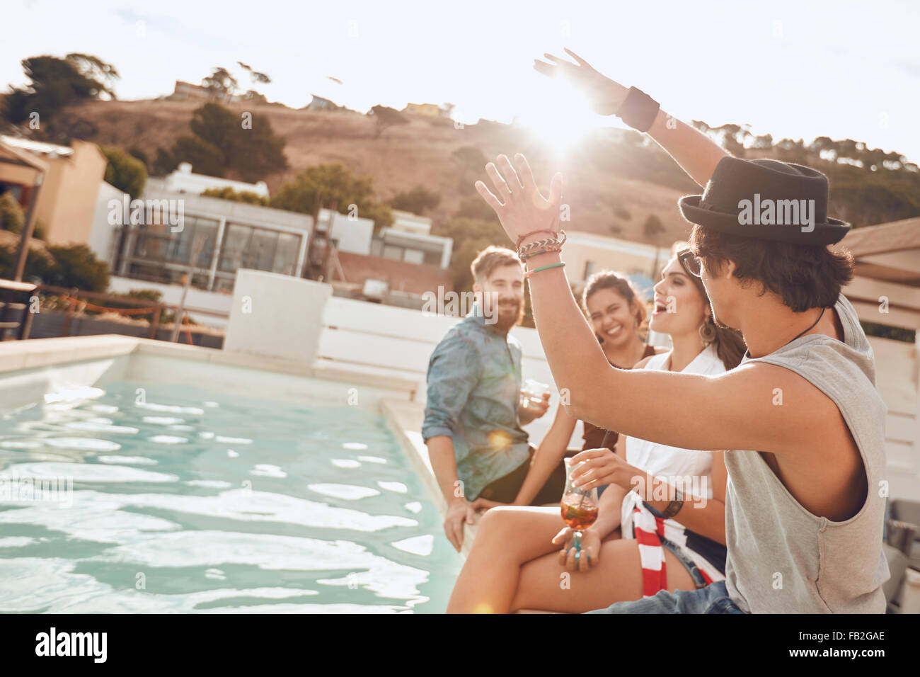 Young people sitting on the edge of the pool enjoying a party. Young woman singing during a the party. Multiracial friends havin Stock Photo