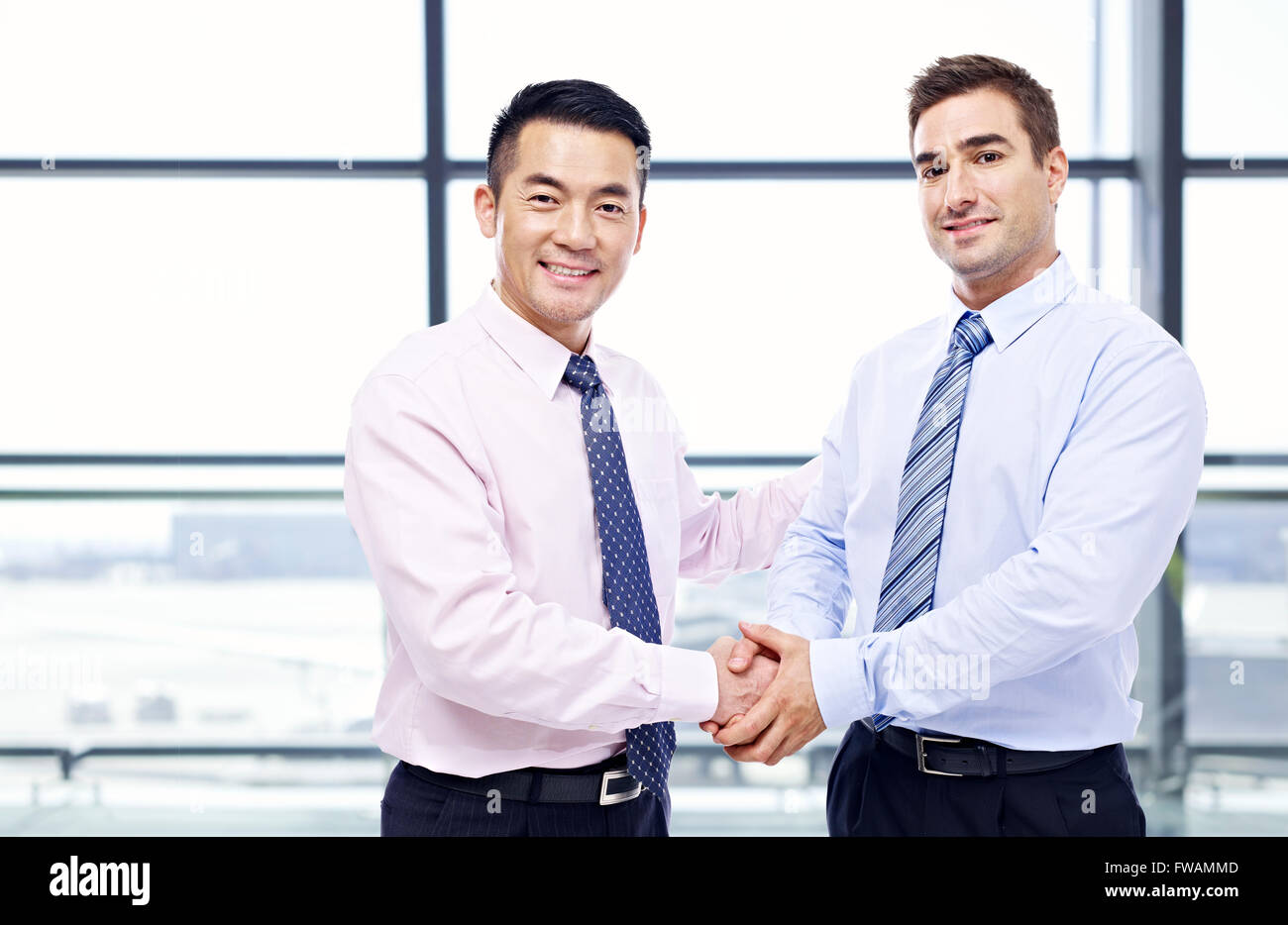 asian and caucasian businessmen shaking hands at airport. Stock Photo