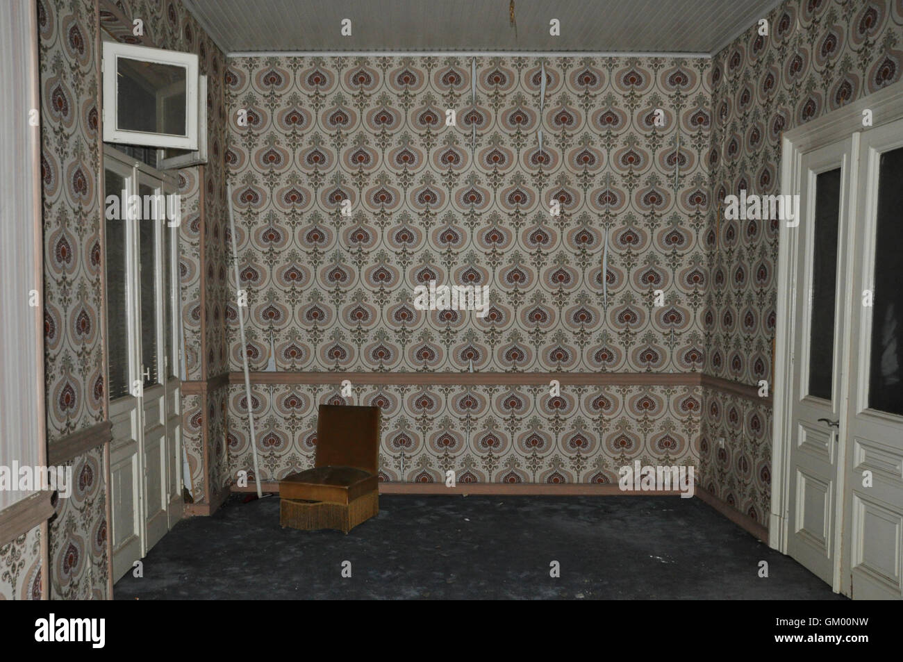 Vintage chair and wall with retro wallpaper pattern in empty living room of an abandoned house. Stock Photo