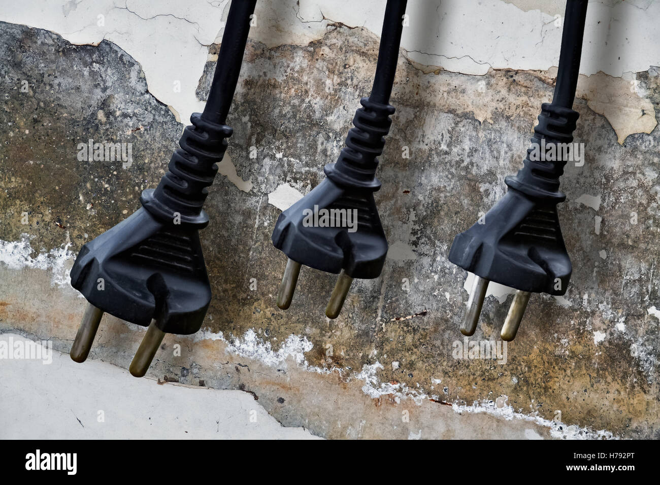 Closeup of three electrical plugs and damaged wall in the background Stock Photo