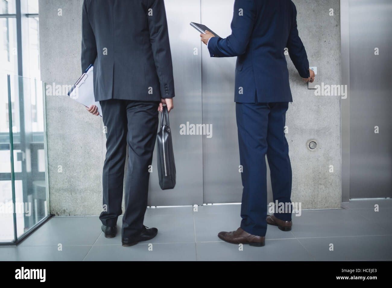 Businessmen standing by lift and pressing button Stock Photo