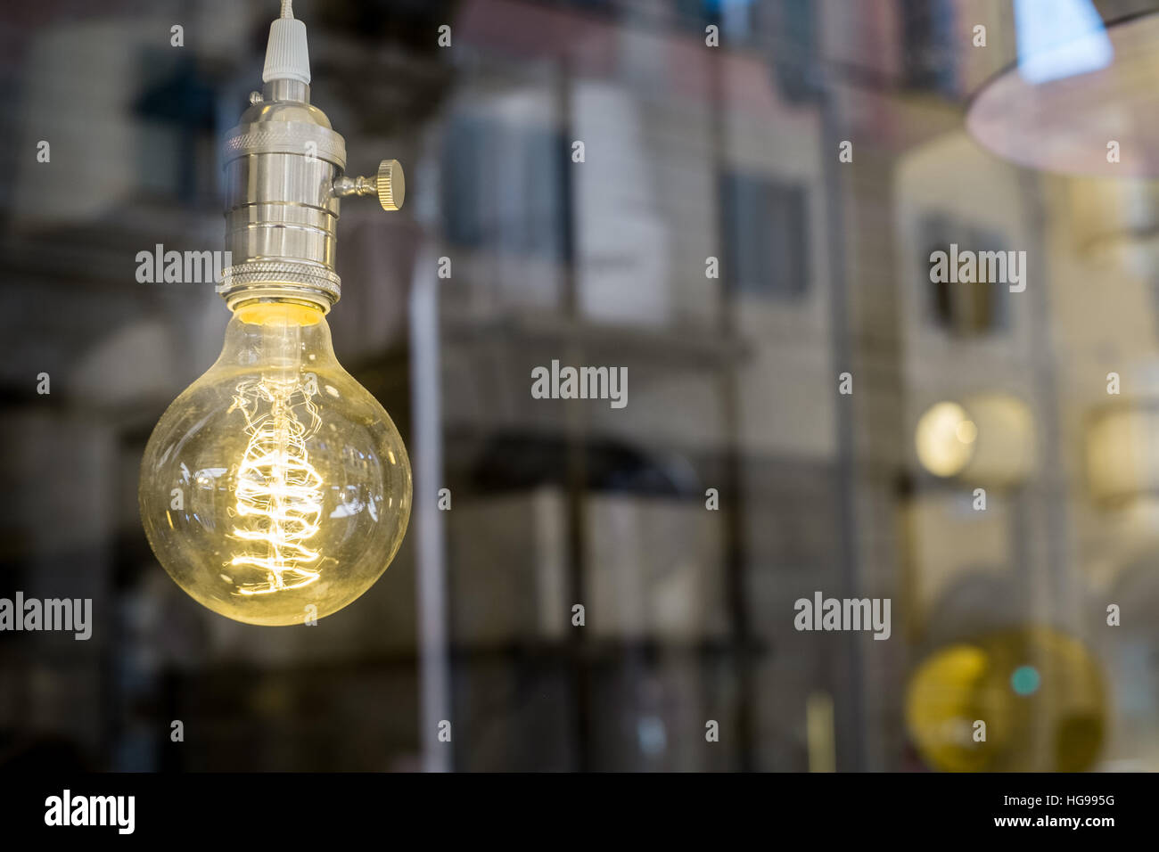 Decorative old Edison style light bulb against blurred urban scene reflecting background Stock Photo