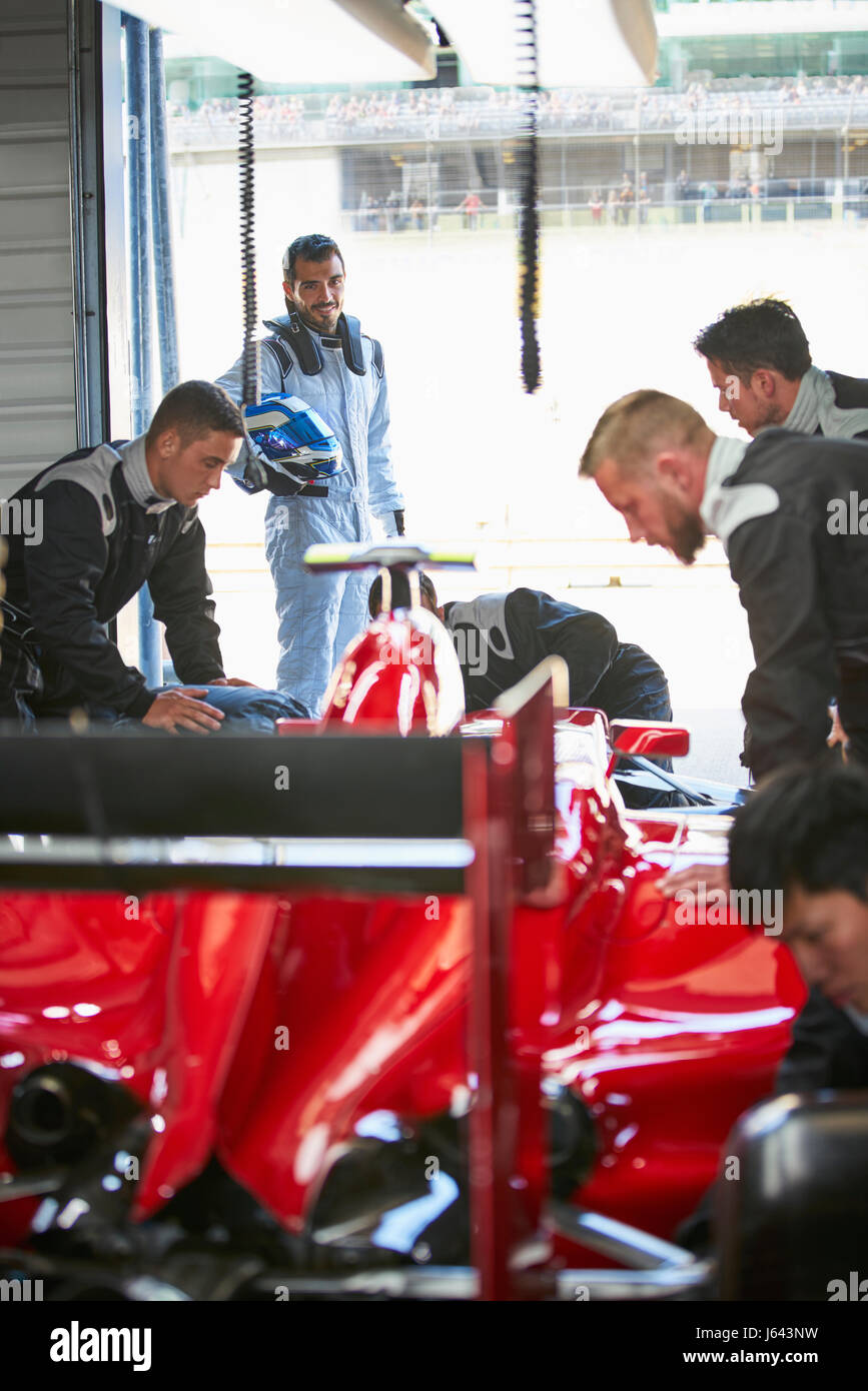 Formula one driver watching pit crew working on race car in repair garage Stock Photo