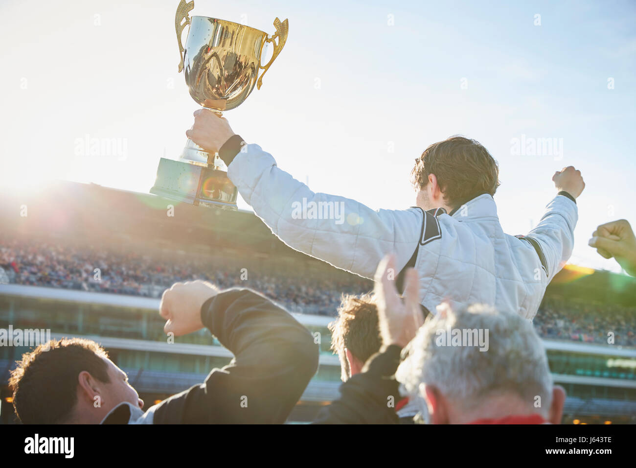 Formula one racing team carrying driver with trophy on shoulders, celebrating victory Stock Photo