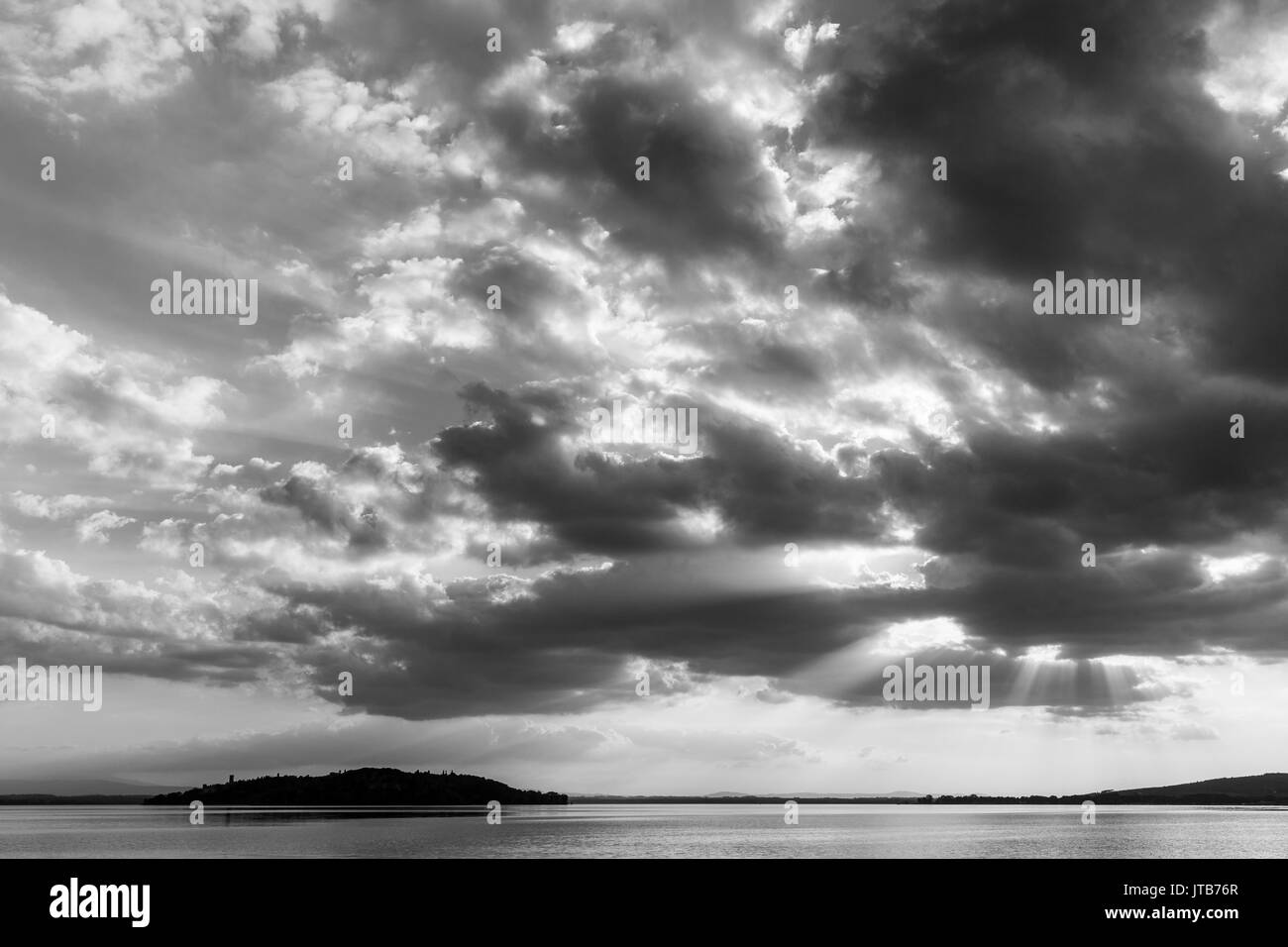 Sun rays coming out through the clouds over an island on a lake Stock Photo