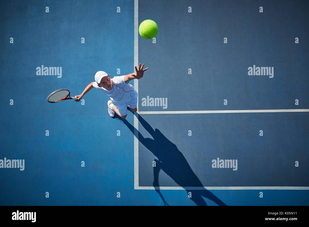 Overhead view of young male tennis player playing tennis, serving the ball on sunny blue tennis court Stock Photo