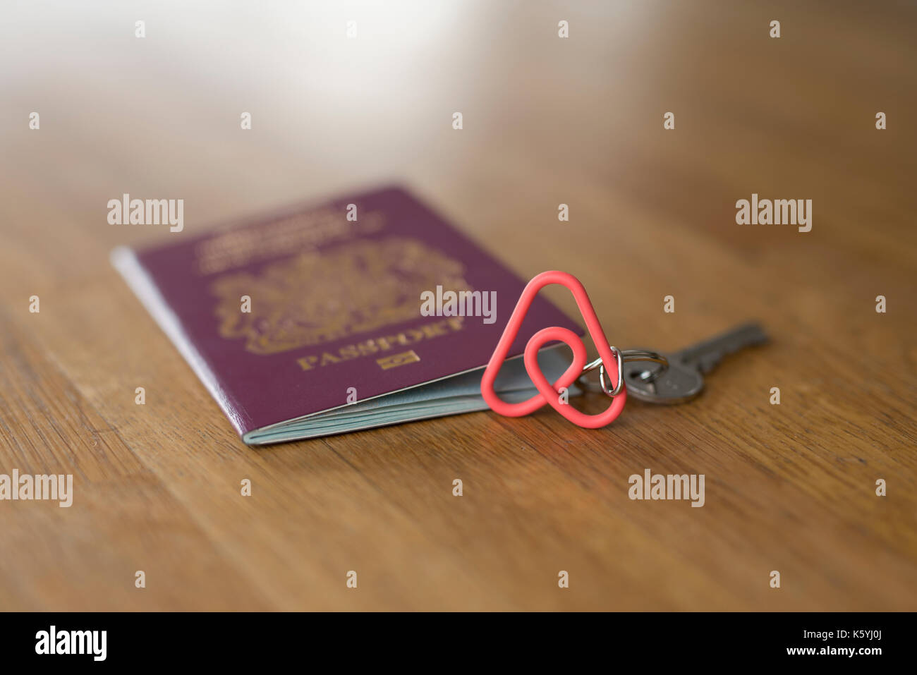 An Airbnb branded keyring along with a British passport on a wooden table top. Stock Photo