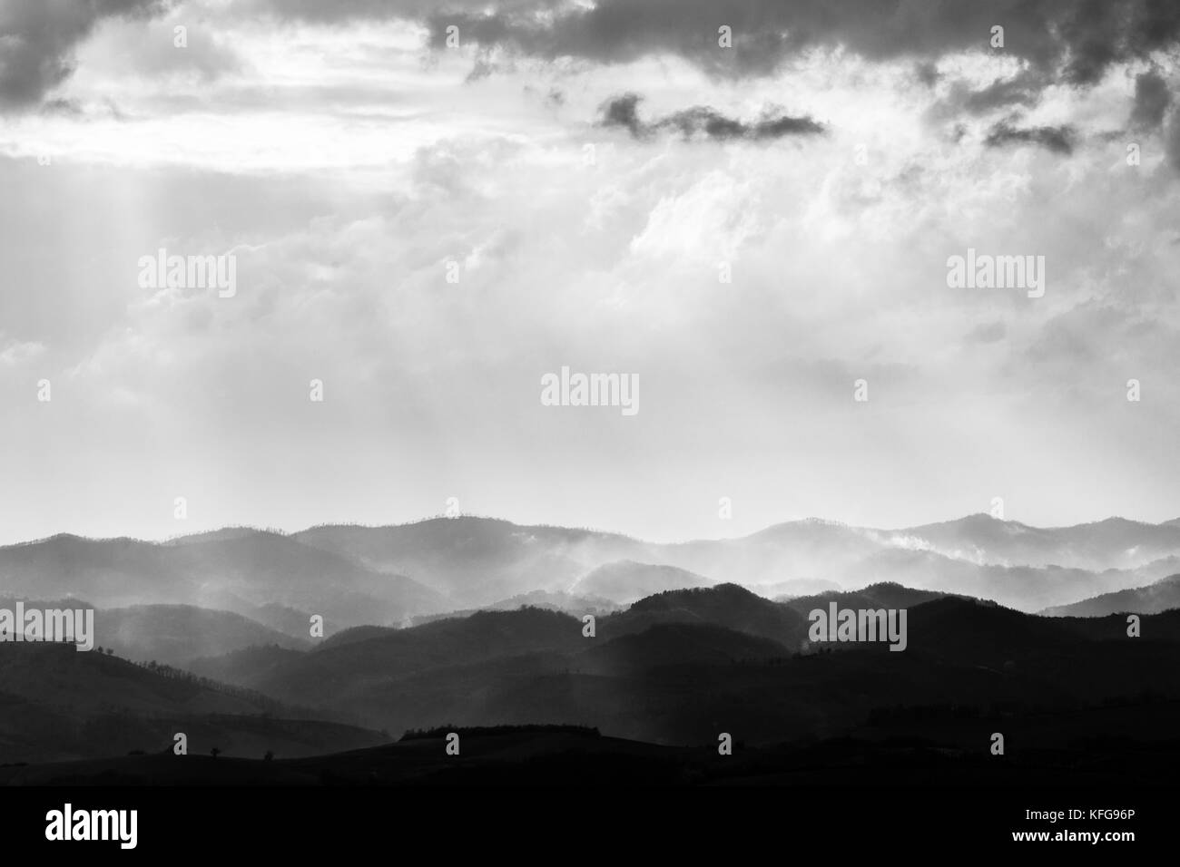 Various layers of hills and mountains with mist between them, with sun rays coming out through the clouds Stock Photo