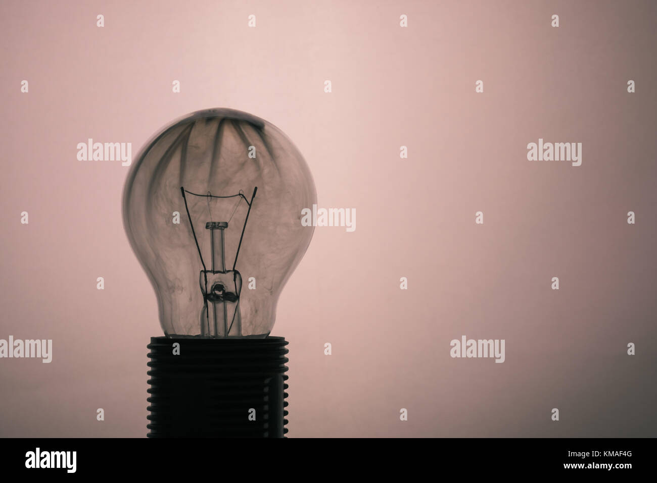 Horizontal photo of single glass bulb placed in the socket on light background. The grey smoke inside was caused by burning wire. The glass is dirty a Stock Photo