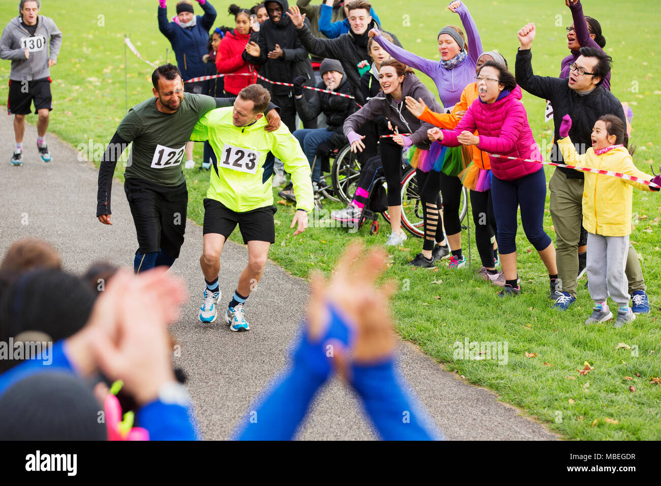 Man helping injured runner finish charity run in park Stock Photo