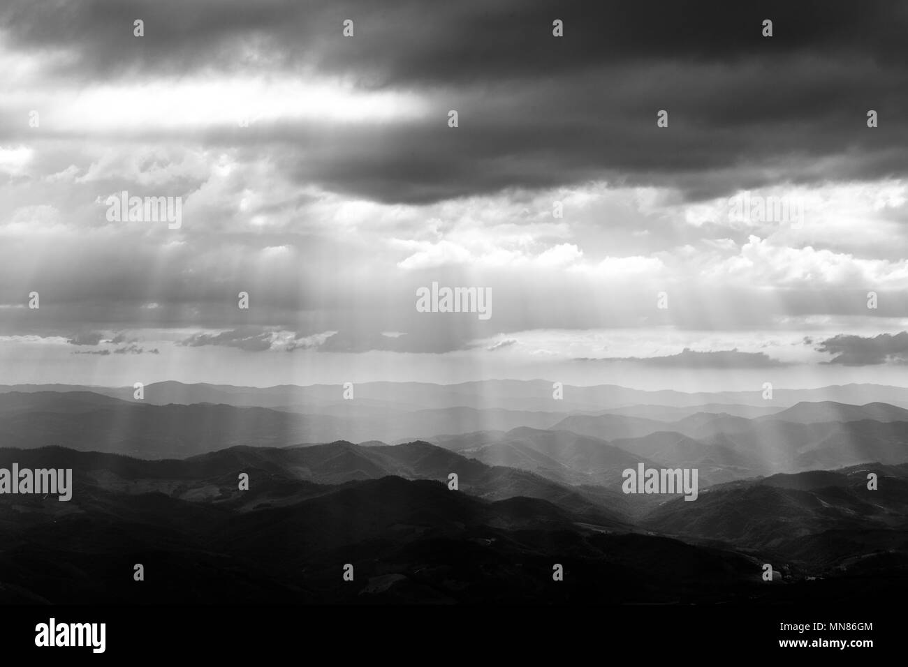 Various layers of hills and mountains with mist between them, with sun rays coming out through the clouds Stock Photo