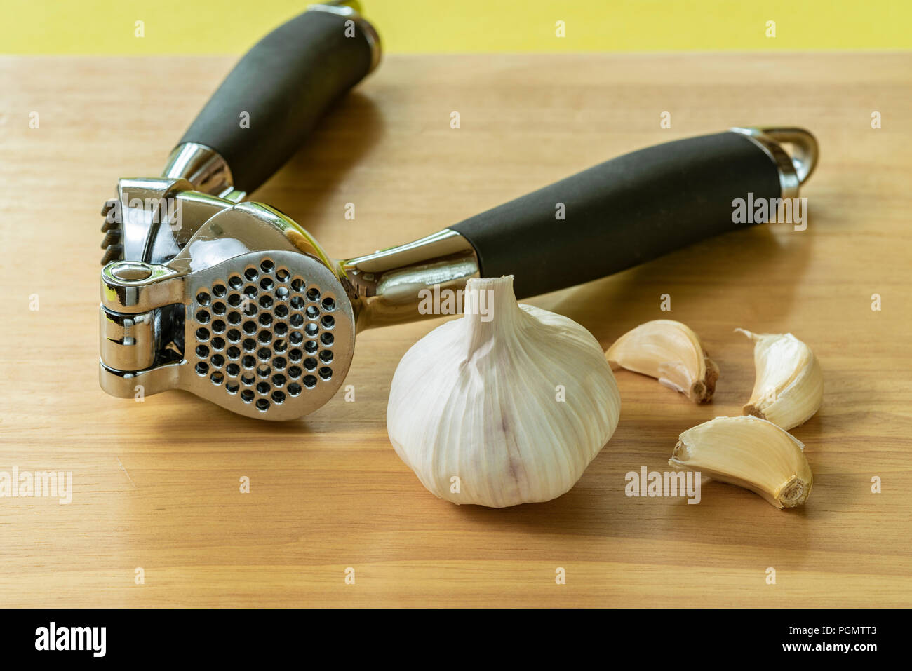 Garlic crusher or press with a bulb and cloves. Stock Photo