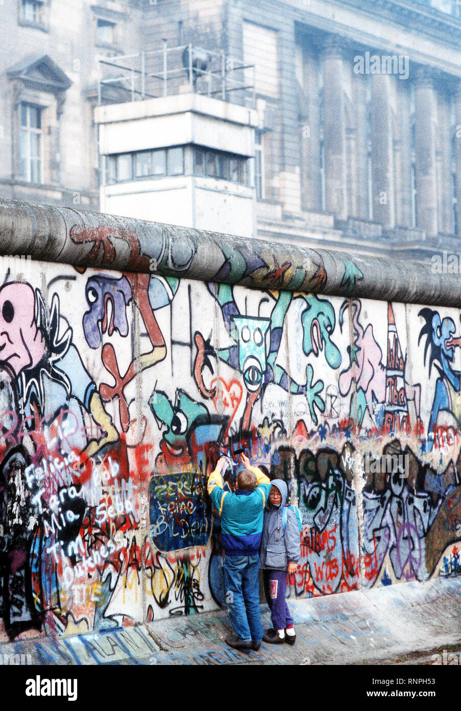 West German children attempt to chip off a piece of the Berlin Wall as a souvenir.  A portion of the Wall has already been demolished at Potsdamer Platz. Stock Photo