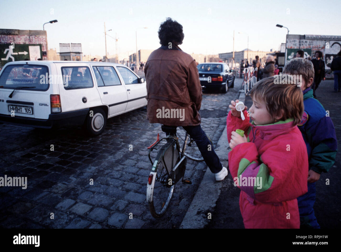 A child blows bubbles at the passing traffic as cars move between East and West Berlin at Potsdamer Platz. Stock Photo