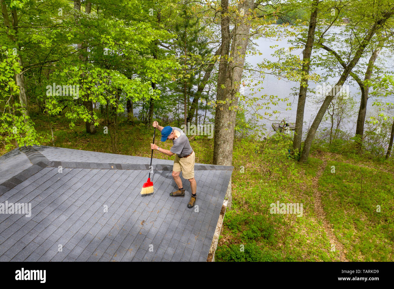 Prairieville, Michigan - A man sweeps winter debris off the roof of a cottage on Stewart Lake. Stock Photo