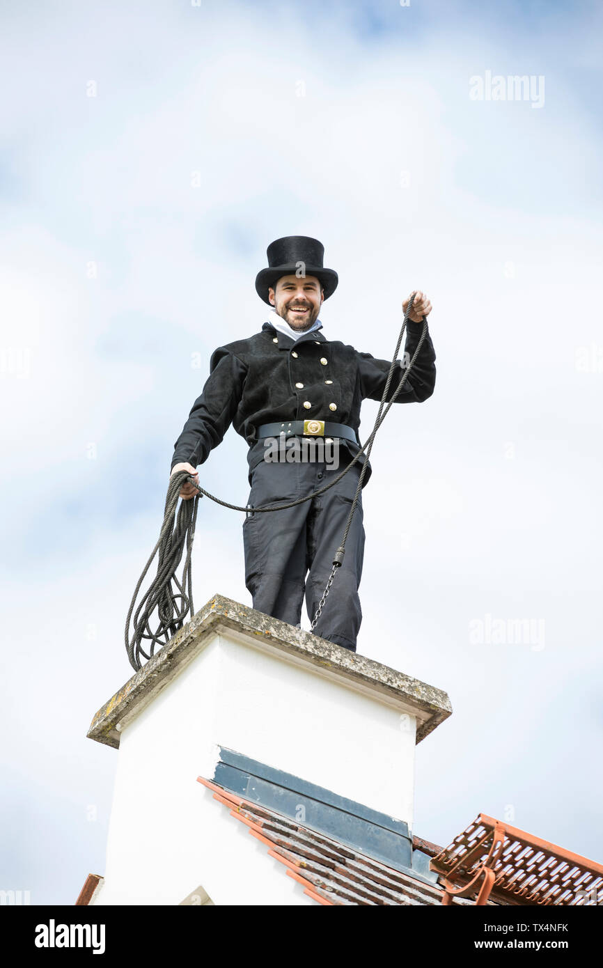 Portrait of smiling chimney sweep working on house roof Stock Photo