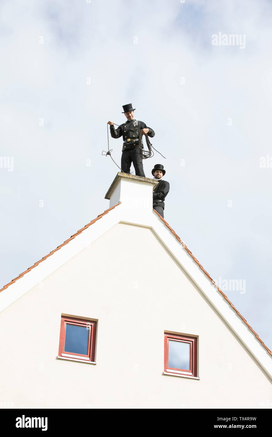 Two chimney sweeps working on house roof Stock Photo