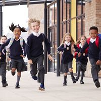 Diverse elementary school children wearing school uniforms running outside of school. Boys girls