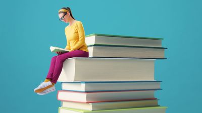 Woman reading while perched on the edge of a blown-up stack of books.