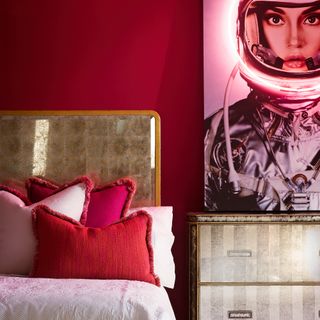 red bedroom with gold rimmed bed and matching chest of drawers, modern artwork, fringed cushions