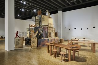 An exhibition area with four different wood tables and large wood boxes in the centre.