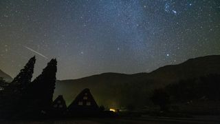 An Orionid meteor streak above the silhouette of Shirakawa-go in Japan. The sky is filled with stars.