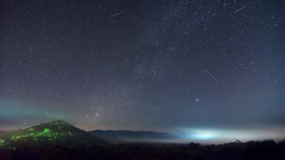 Numerous meteor streaks against a star-studded sky above a forested area in Thailand.