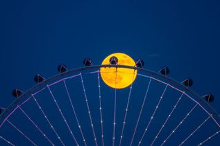 A deep orange sphere behind a circular steel structure with silver spokes