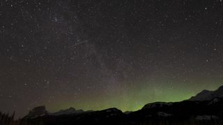 Meteor streaks across the star-studded sky with mountains below.