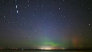 A bright meteor streak in the top left of the image is accompanied by an impressive aurora below, with ribbons of blue and green light "dancing" in the sky.