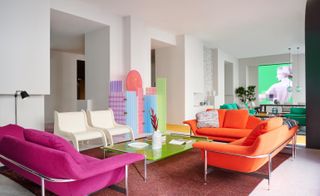 Cassina showroom Milan with multi-coloured sofas (red, organge), and two white chairs, around a glass table with tableware. Green sofas are on the other side of the room.