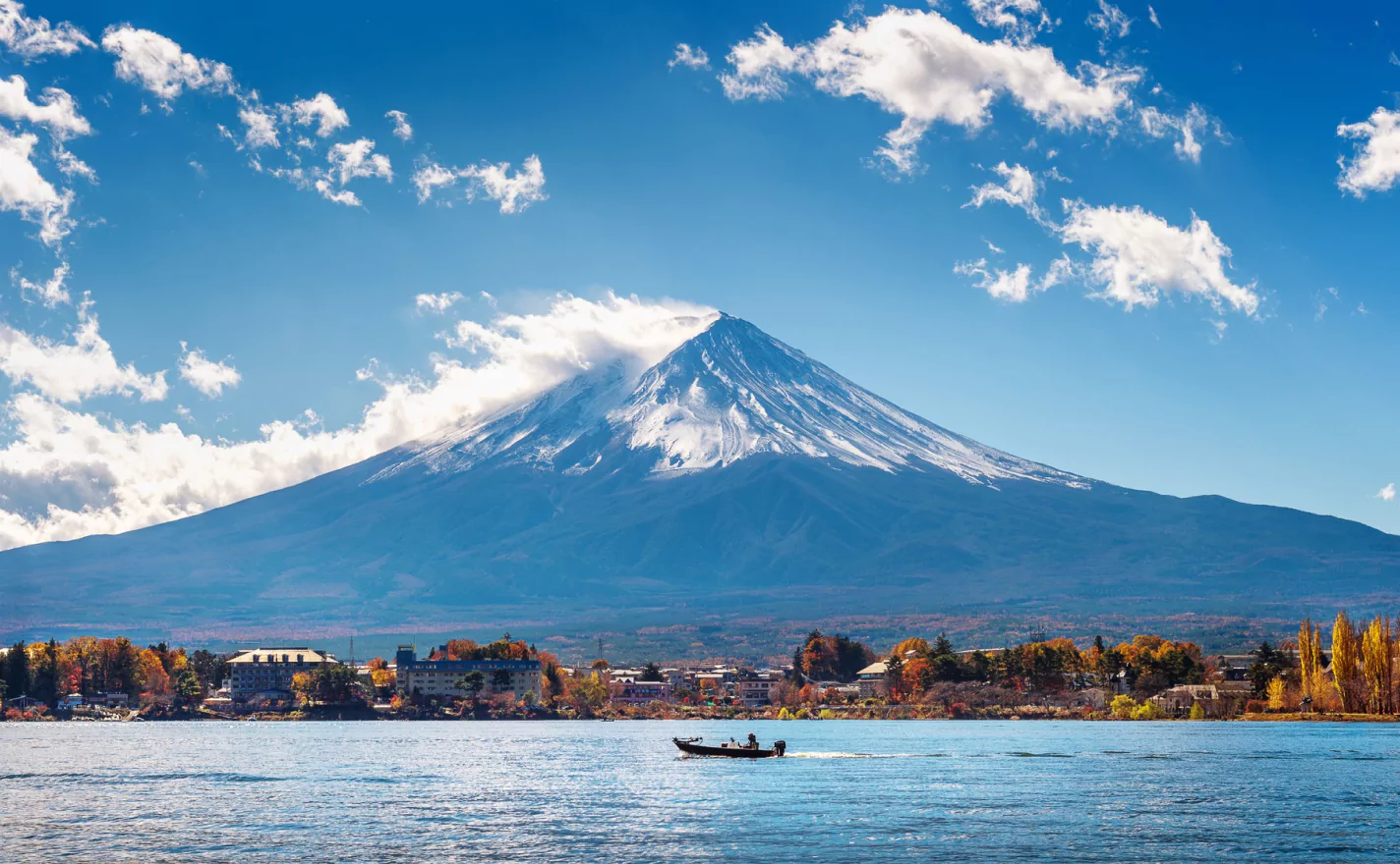 A boat navigates the calm waters, framed by a towering mountain