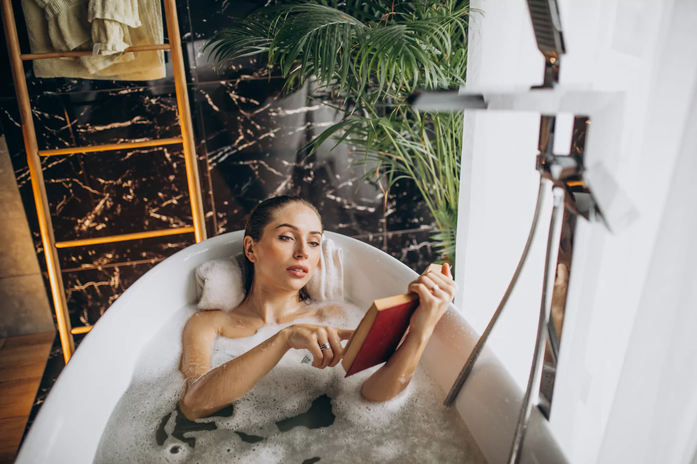 A woman sits in a bathtub, absorbed in a book