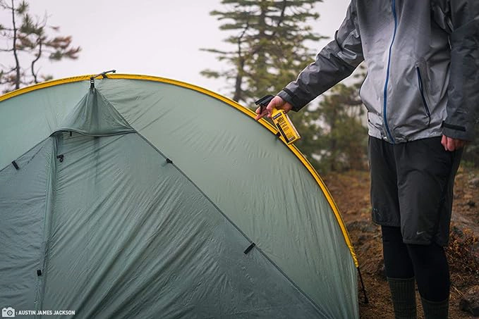 A person spraying a camping tent in the woods with Sawyer premium Permethrin fabric treatment insect repellent