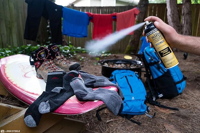 A person spraying Sawyer Permethrin aerosol spray insect repellent on hiking boots and socks in their backyard