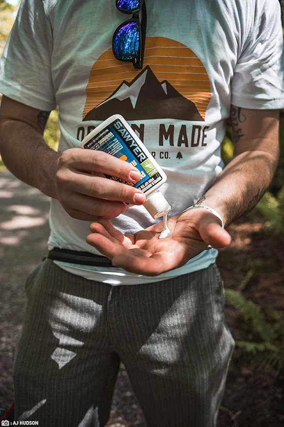 A person squeezing Sawyer picaridin insect repellent lotion into hands in the forest