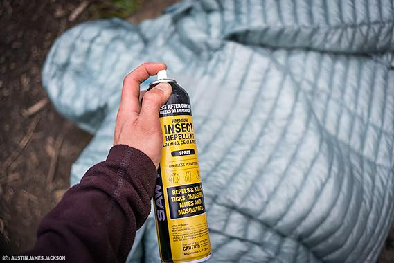 A person spraying Sawyer premium Permethrin insect repellent on a down jacket in the forest