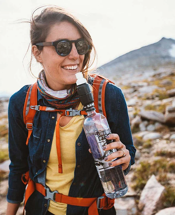 Makayla Crist using a Sawyer micro squeeze water filter on a Smartwater bottle whilte hiking