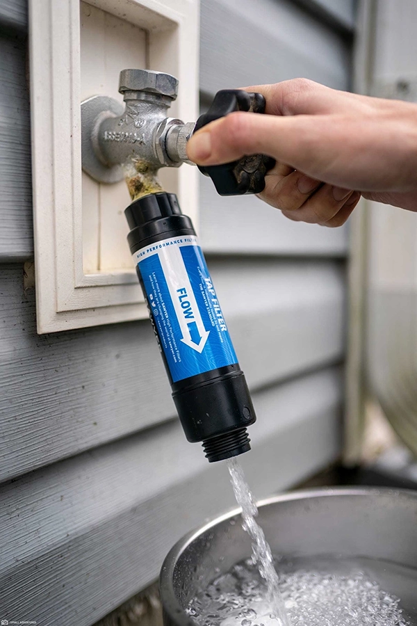 A Sawyer tap filter filtering water on an outdoor spigot on the side of a house