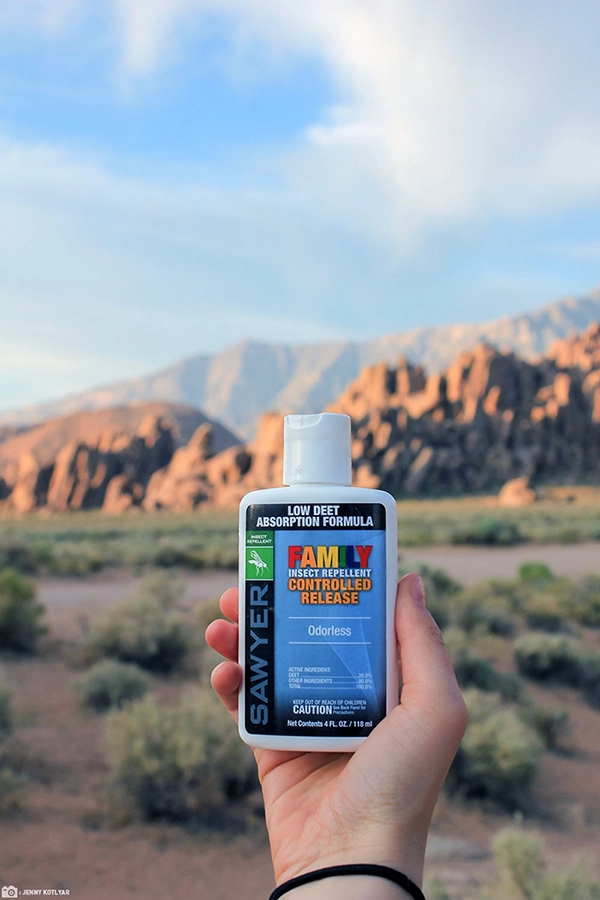 A hand holding a bottle of Sawyer family insect repellent controlled release topical lotion in front of mountains