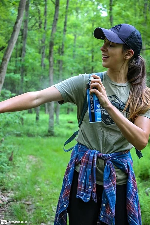 A woman spraying Sawyer picaridin insect repellent on arms in the forest