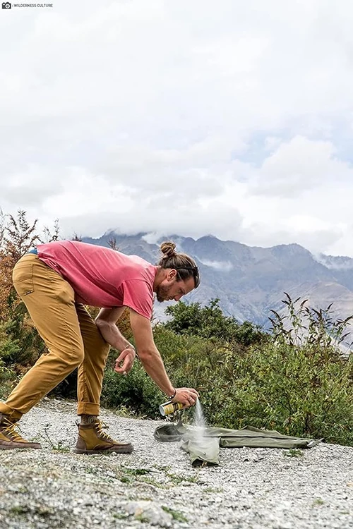 A man spraying a jacket with Sawyer Permethrin insect repellent in the mountains