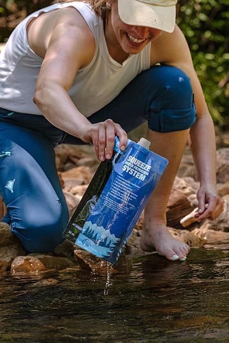 A woman filling a Sawyer squeeze water filtration pouch from a stream of water