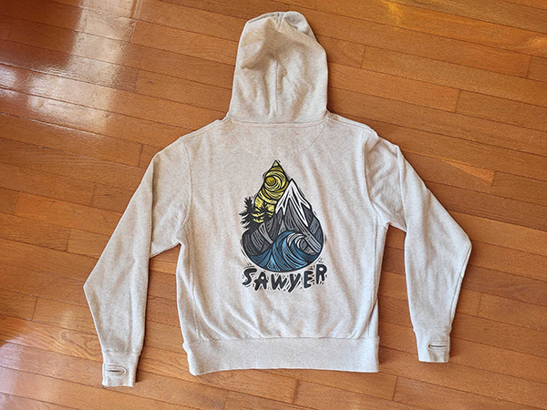 A oatmeal colored hoodie with Woosah Sawyer illustration on back