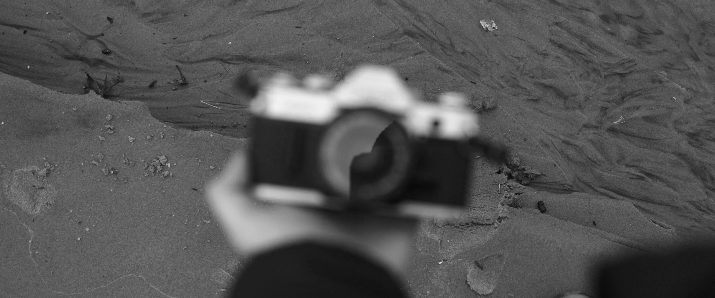 Black and white VSCO filter on a hand holding an out of focus camera with sand in the background